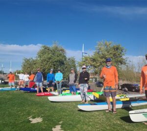 Group of people with paddleboards on grassy field. Tempe Town Lake Fitness Paddle.